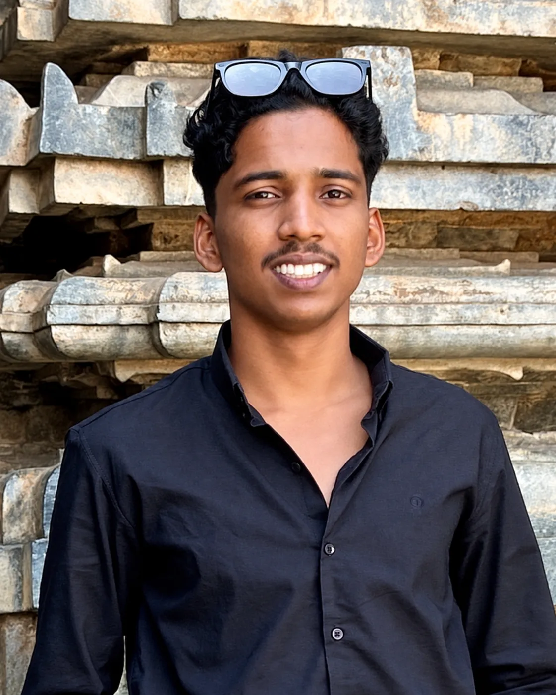 Ahammed Nibras smiling in front of a carved stone wall.